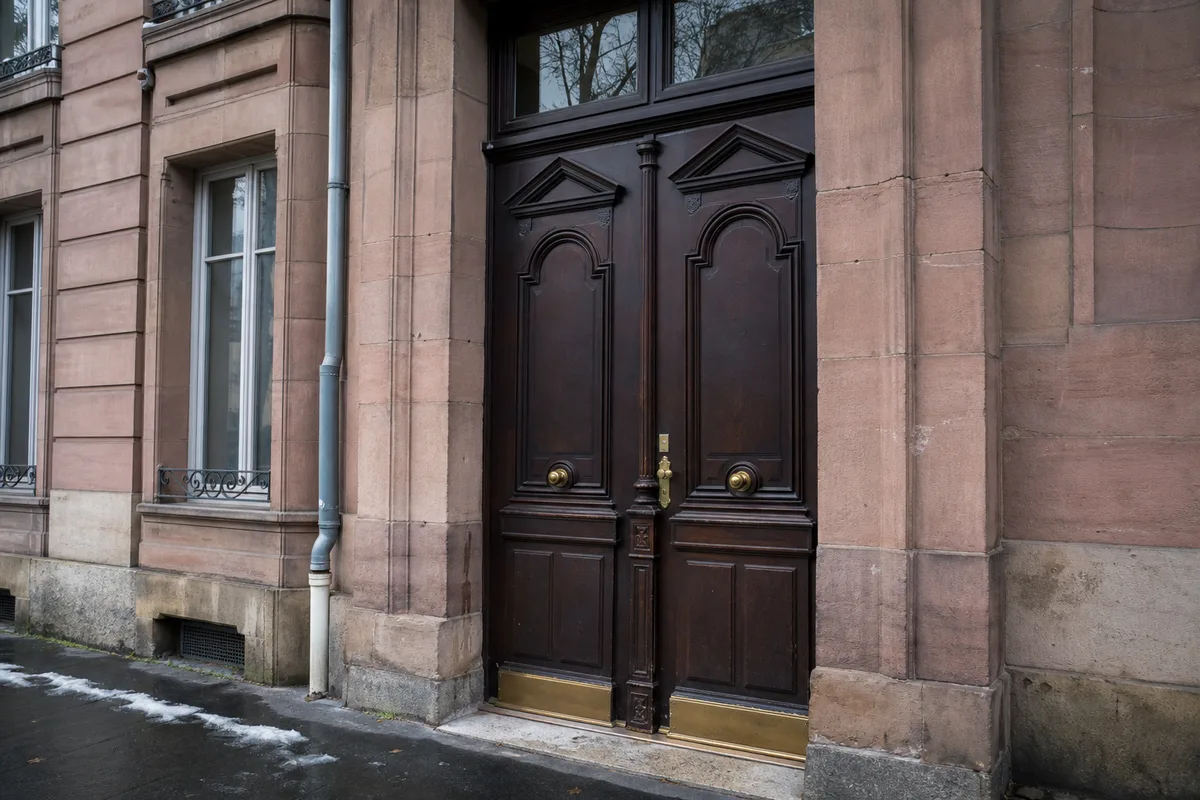 Porte d’immeuble ancien en grès rose à Belfort, serrure et poignée en laiton, lumière hivernale