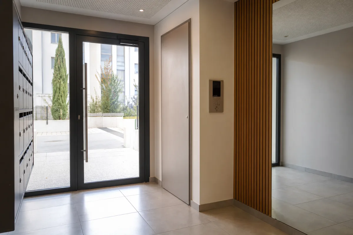 Hall d’entrée d’un immeuble récent à Istres, interphone et porte vitrée, lumière neutre